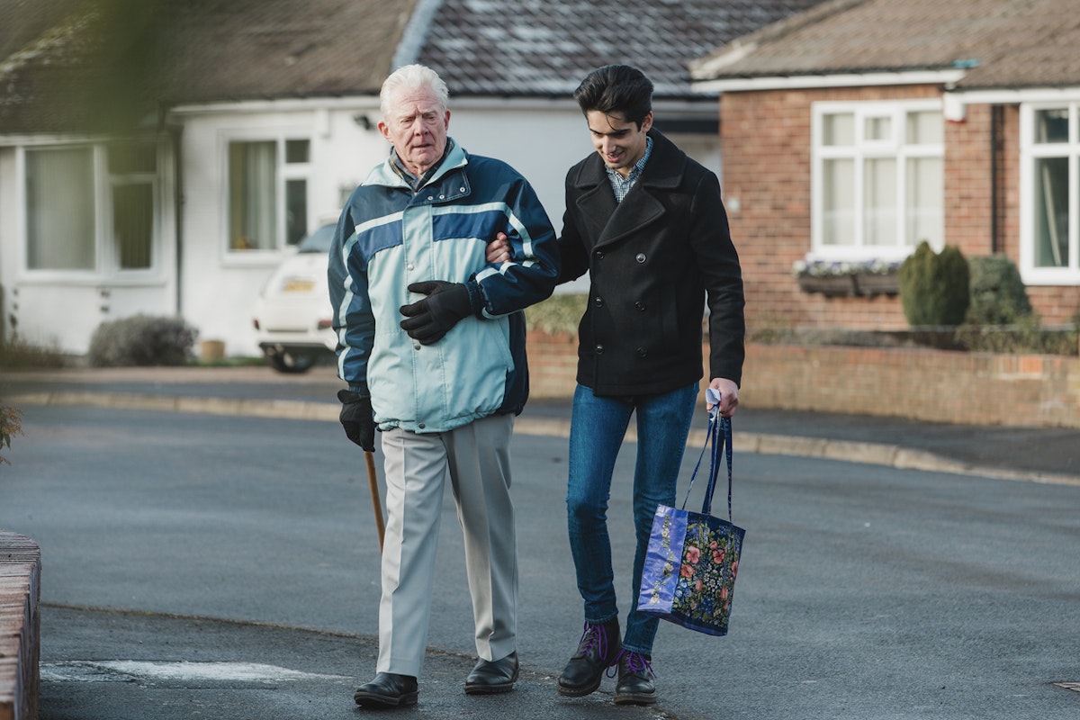 Teenage boy is walking back from the shop with his grandparent. He is carrying the shopping bag and they are linking arms.